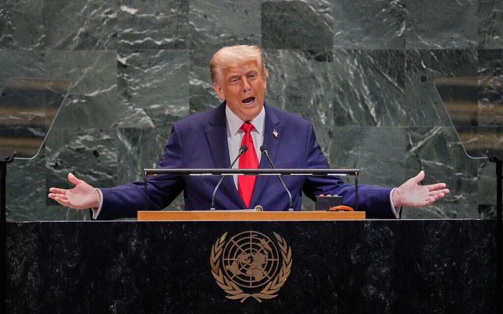 President Donald Trump stands at the podium addressing the United Nations General Assembly, with a binder of speech notes open in front of him.
